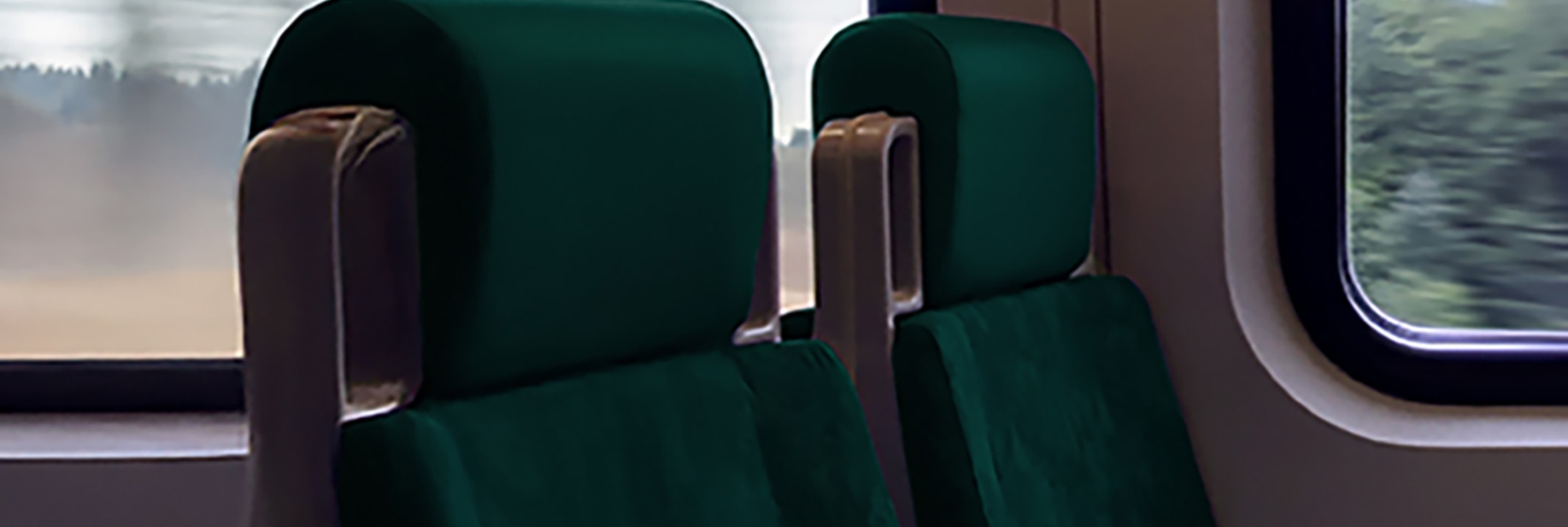 Two empty green train seats sit side by side, bathed in soft light, as the blurred scenery rushes past the windows in motion.
