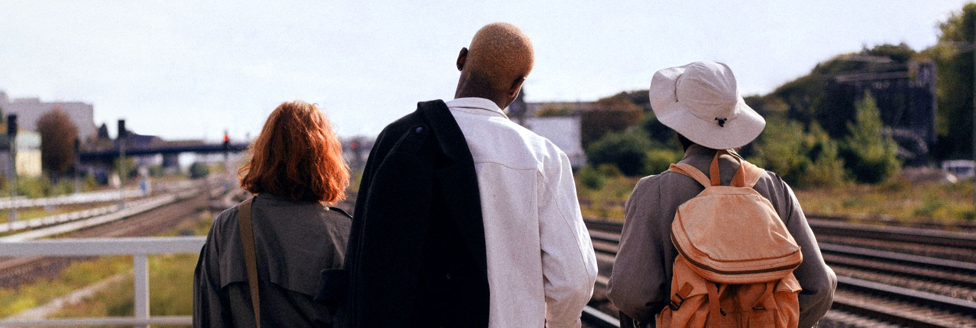 3 persons on a train platform looking in the distance