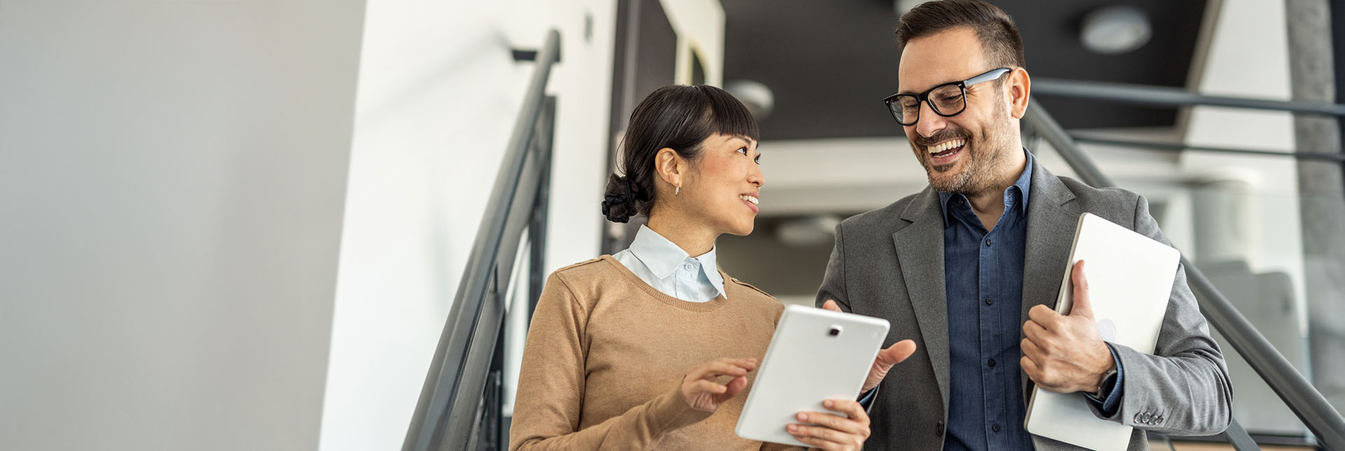 A professional woman and man walking down the stairs holding tablets