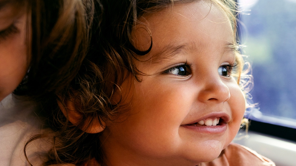 A child in an orange shirt sits near a train window.