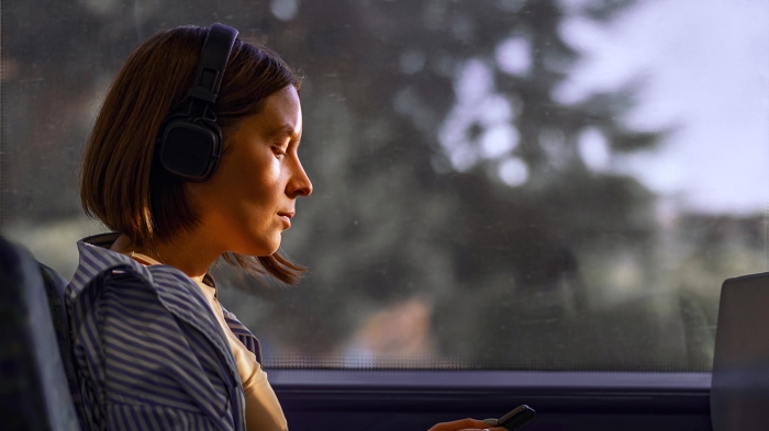 A person with headphones sits by a train window, holding a smartphone.