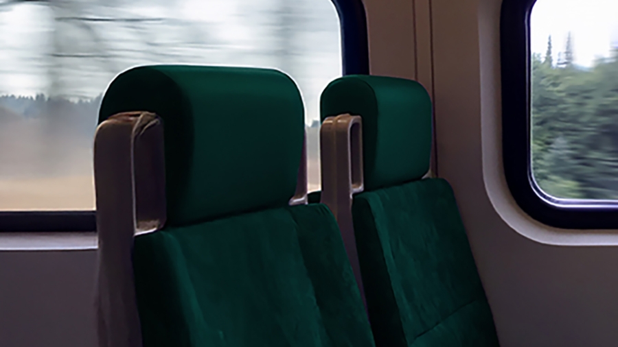 Two empty green train seats sit side by side, bathed in soft light, as the blurred scenery rushes past the windows in motion.