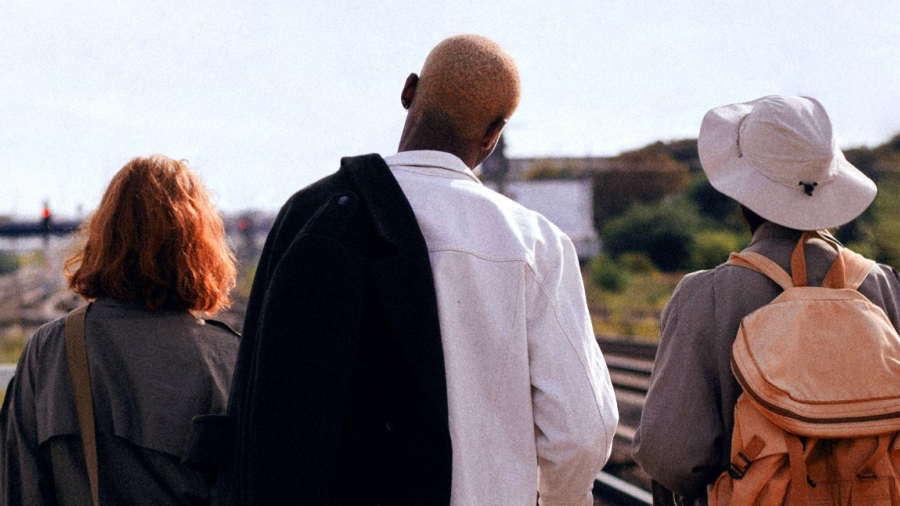 3 persons on a train platform looking in the distance