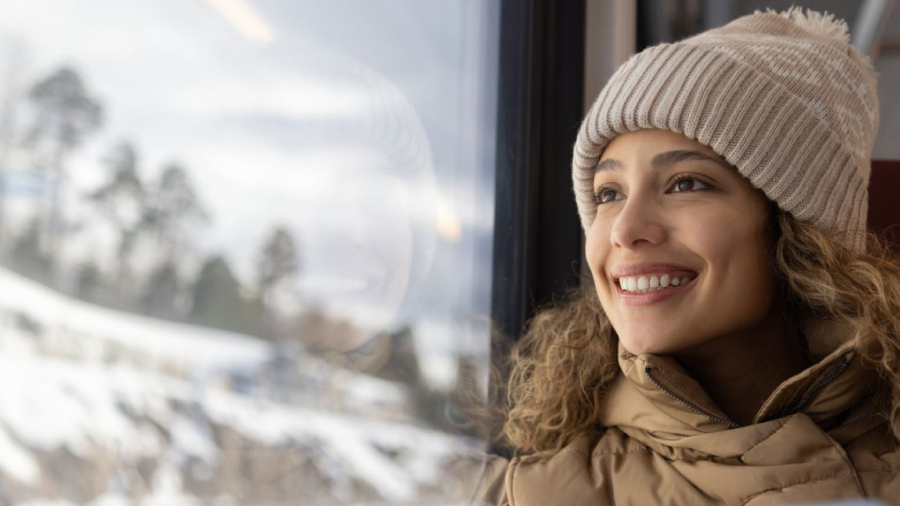 Woman with winter clothes on smiling while looking outside from a train