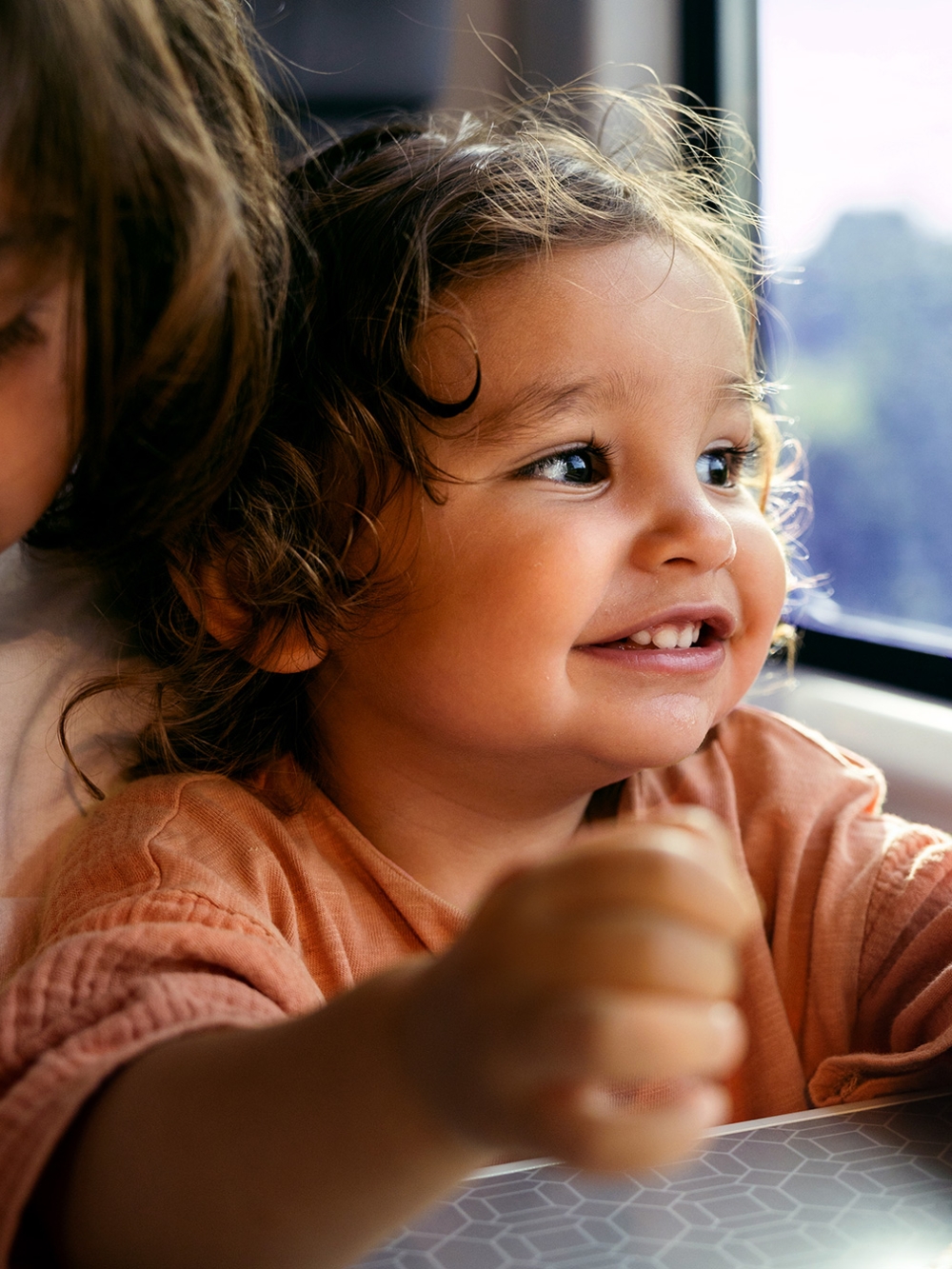 A child in an orange shirt sits near a train window.