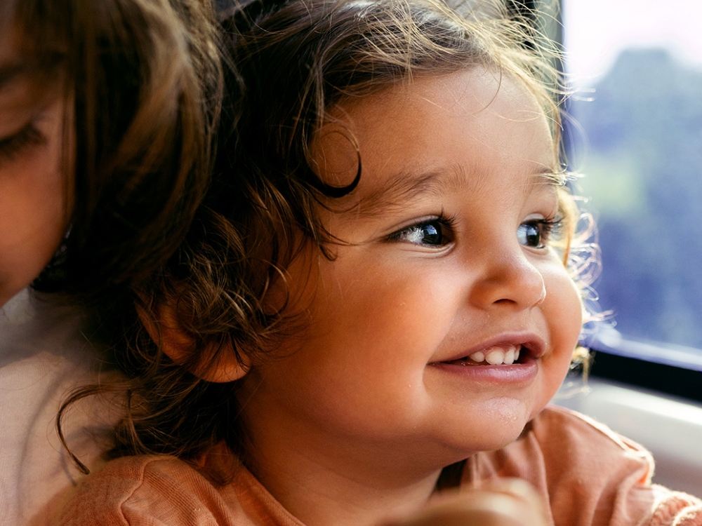 A child in an orange shirt sits near a train window.