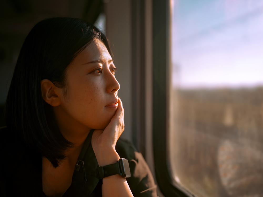 A person in a black shirt looks out of a train window, resting their head on their hand.