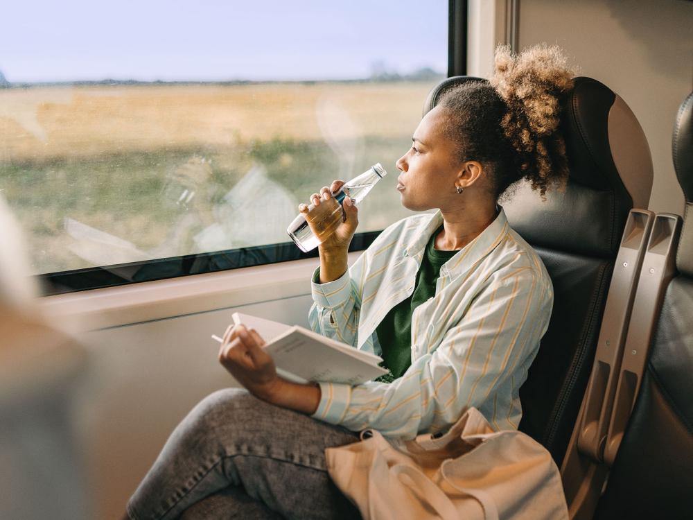 Woman with a drink and a book on the train looking by the window