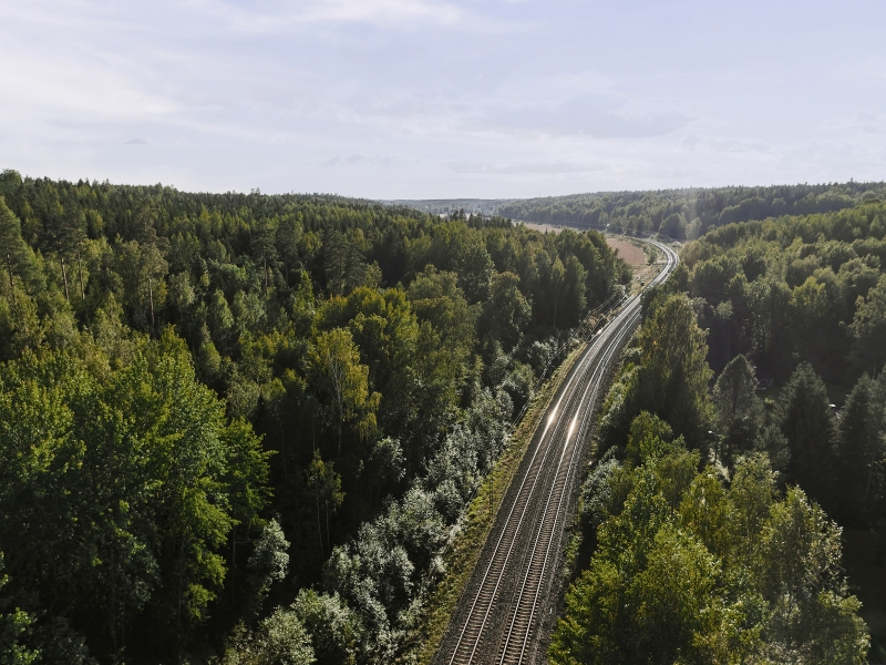 A railway track runs through a dense forest under a partly cloudy sky.